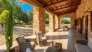 An outdoor patio with stone columns, wicker furniture, and a cactus plant.