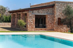 Ein Gebäude aus Stein mit einem Pool, das eine überdachte Terrasse und einen kleinen Baum zeigt.
