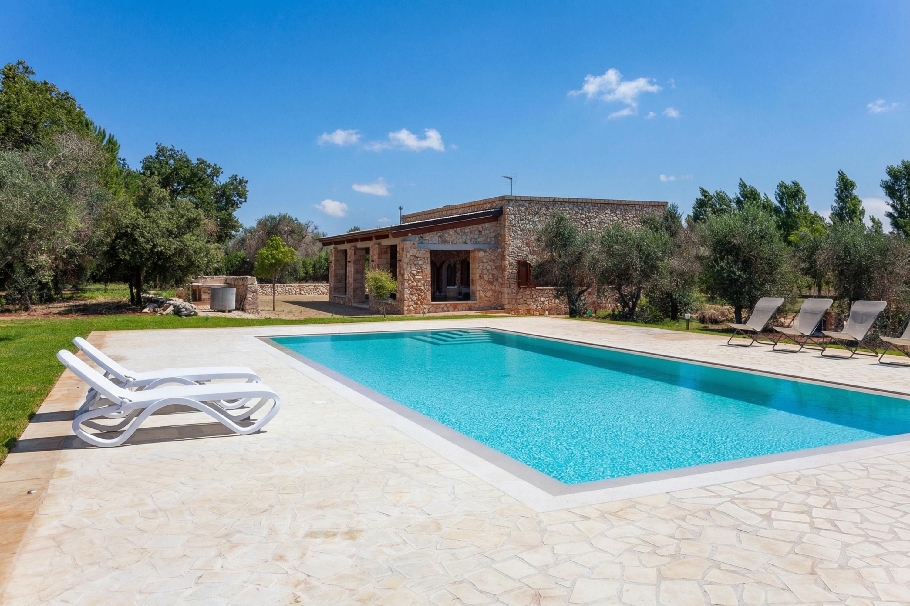A swimming pool with lounge chairs, a stone building, and trees.