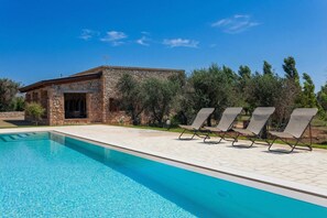 A swimming pool with lounge chairs, a stone building, and surrounding greenery.