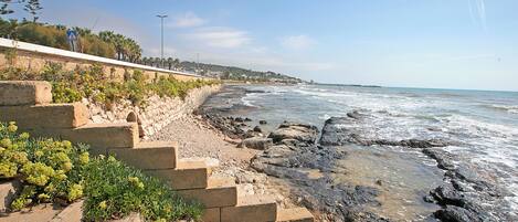 A coastal walkway with stone steps leading to the beach, overlooking the ocean.