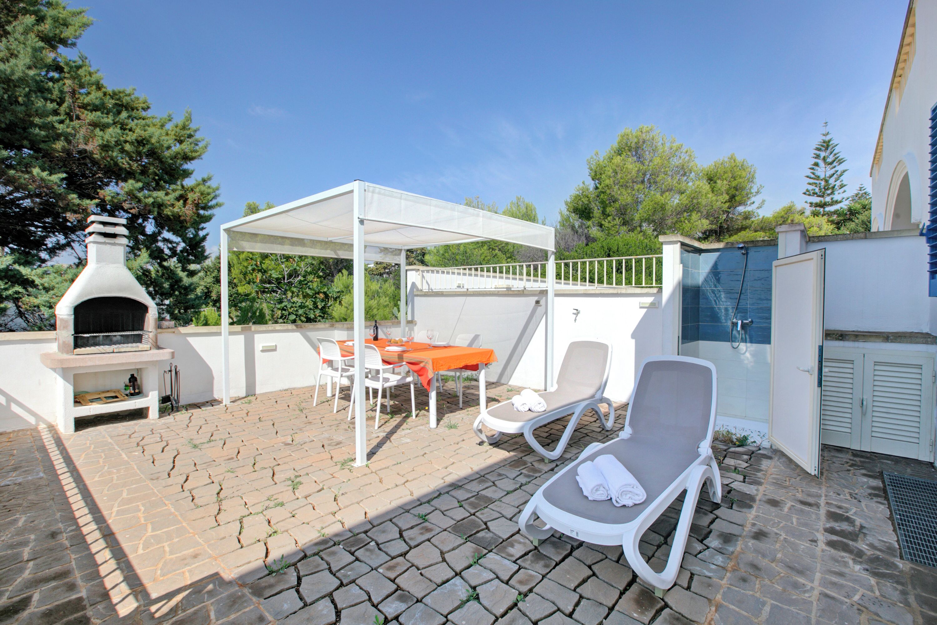 An outdoor patio with a barbecue grill, a covered seating area, and lounge chairs.
