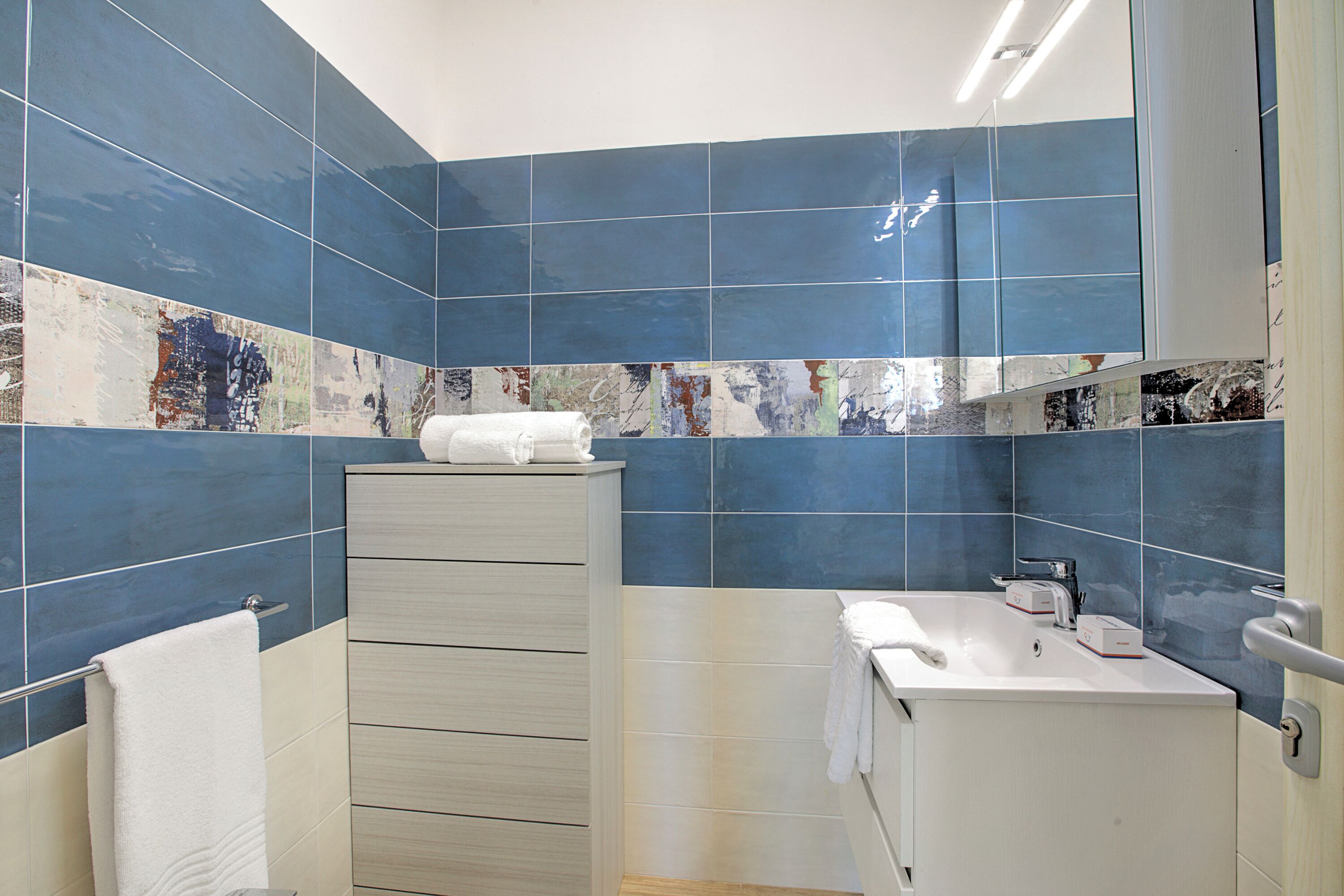 Une salle de bain avec des carreaux bleus, un lavabo blanc et un porte-serviettes.