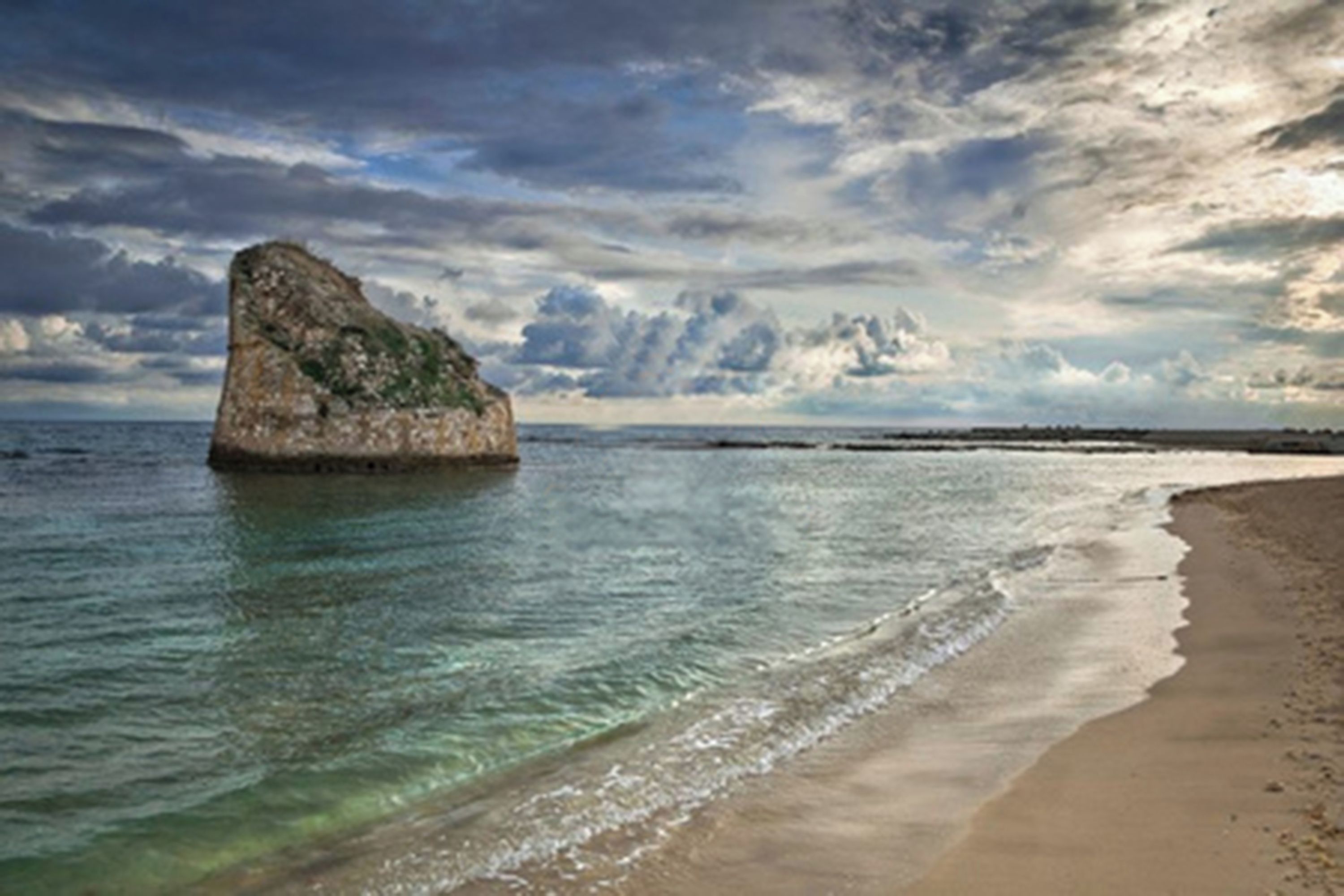 A coastal scene with a prominent rock formation in the water and a sandy beach.