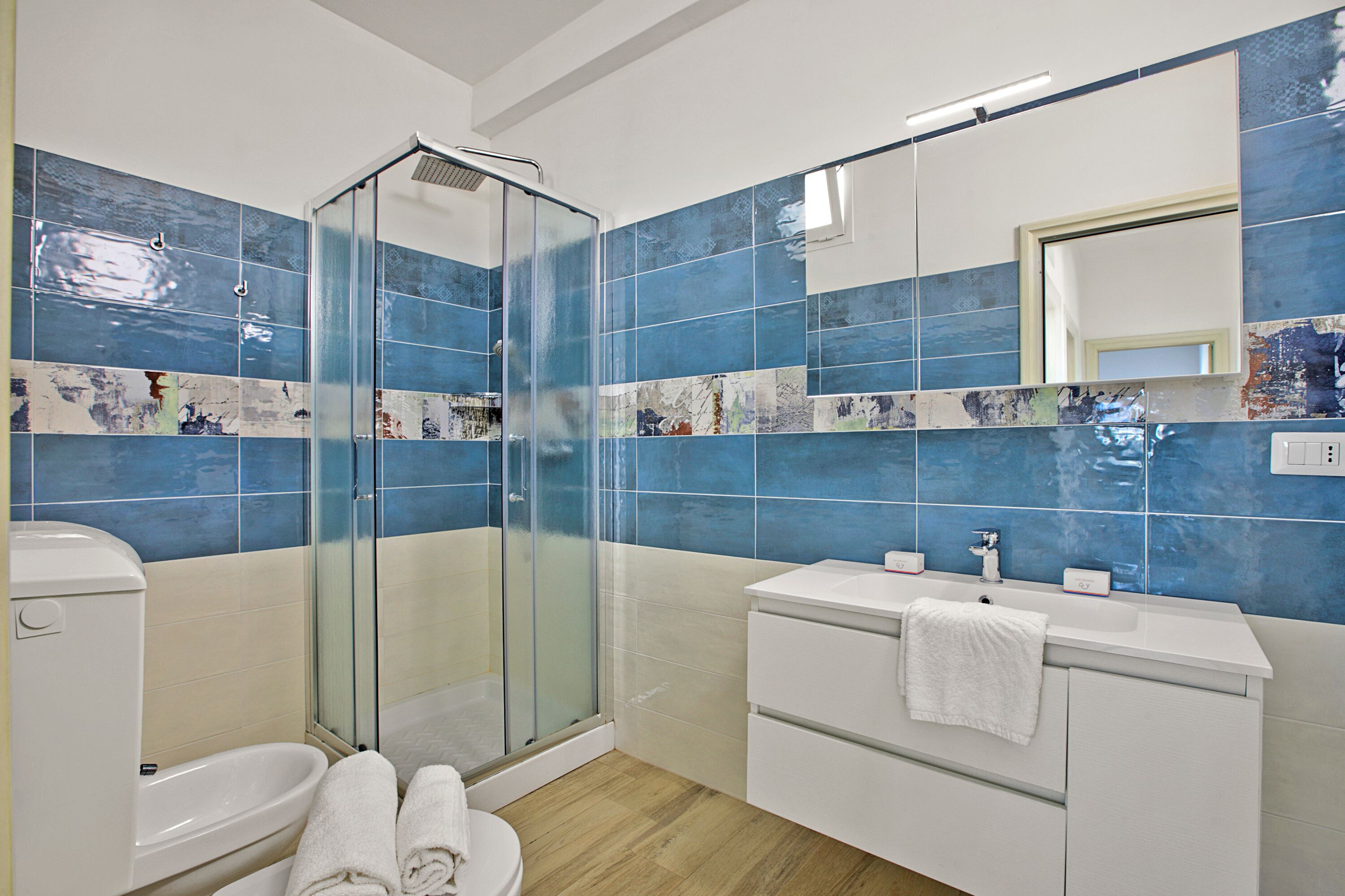 A modern bathroom with a glass shower enclosure, a white sink, and a large mirror.