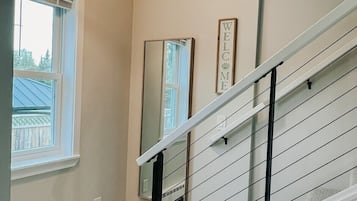 Uma escadaria com corrimão branco, luminária trançada e um letreiro 'WELCOME' na parede.