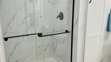 Une douche fermée par des parois de verre, avec un cadre noir et un mur recouvert de carreaux de marbre.