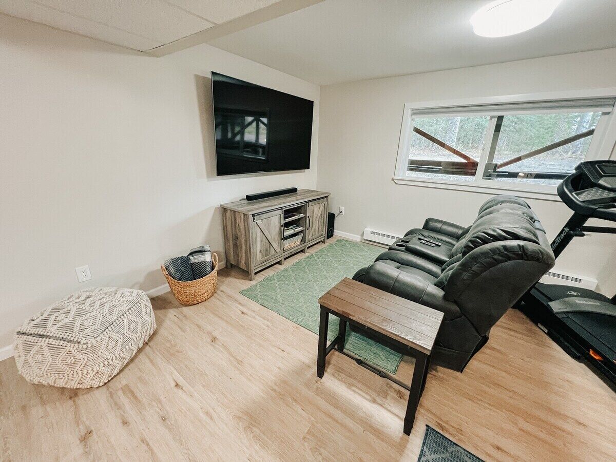 A living room with a television, a sofa, a treadmill, and a wooden floor.