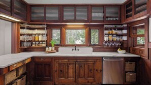 A kitchen with wooden cabinets, a stainless steel dishwasher, and a window with a view of trees. - Spacious 5BR Stowe Resort | Forest & River Views (Stowe)