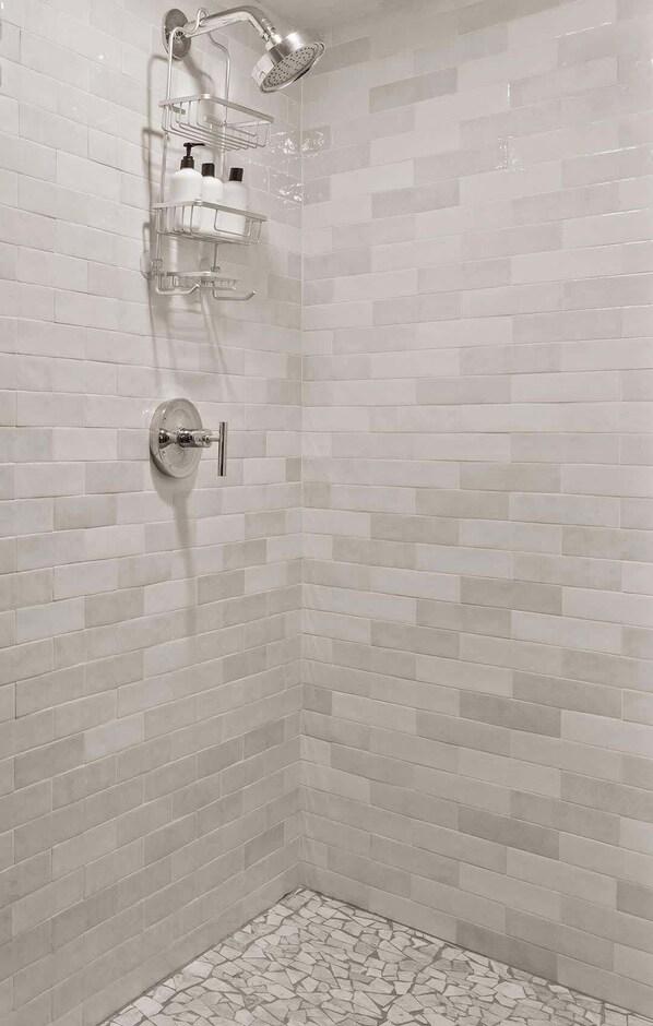 Een douche met een handdouche, een glazen plankje met toiletartikelen en een betegelde vloer.