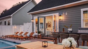 A poolside area with lounge chairs, a wooden table, and a bar area with chairs and a decorative vase. - Spacious Savannah Home | Pool, Spa & Greens (Savannah)