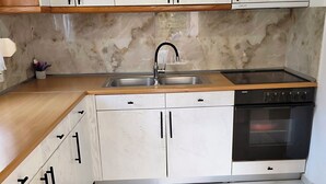 A kitchen with white cabinets, a black stove, and a marble backsplash. - Kastraki House with a view (Kalabaka)
