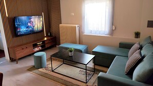 A modern living room with a flat-screen TV, a sofa, a coffee table, and a window with curtains. - Kastraki House with a view (Kalabaka)