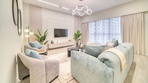 Un salon moderne avec un ensemble de canapés, un téléviseur à écran plat et une grande fenêtre agrémentée de rideaux.