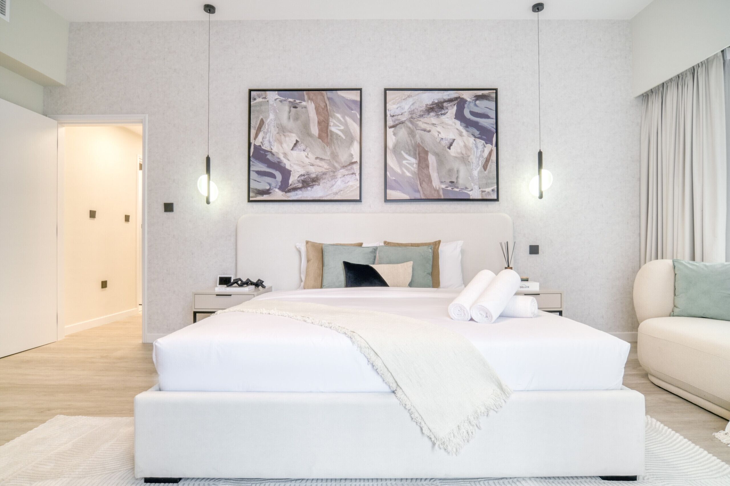 Ein modernes Schlafzimmer mit einem großen Bett, zwei Wandleuchten und einem abstrakten Kunstwerk an der Wand.