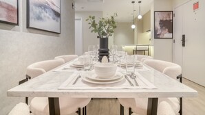 Un coin repas avec une table en marbre, des chaises blanches et un vase contenant des plantes vertes.
