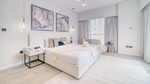 Une chambre à coucher moderne avec un grand lit, des tables de chevet, une petite table, une chaise et un luminaire au plafond.