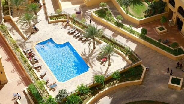 Vue aérienne d’un complexe hôtelier doté d’une piscine centrale, de palmiers et d’une terrasse ensoleillée.