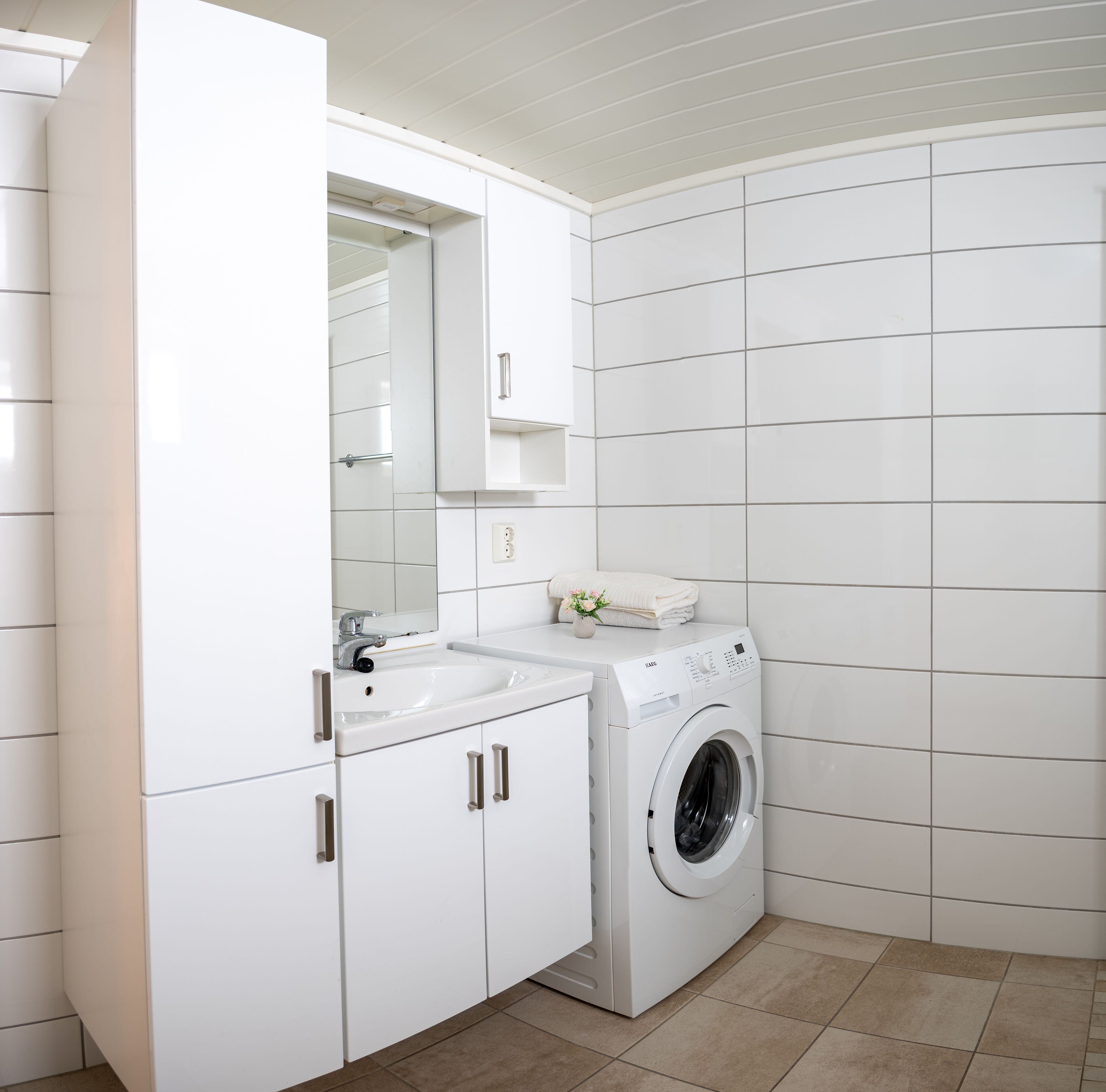 A modern bathroom with white cabinetry, a sink, a mirror, and a front-loading washing machine.
