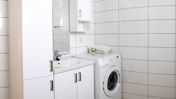A modern bathroom with white cabinetry, a sink, a mirror, and a front-loading washing machine.