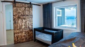 A bedroom with a wooden wardrobe, a window with a view, a bed, and a small crib.