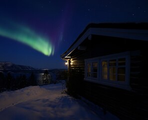 A log cabin with a snow-covered ground and a view of the night sky with the aurora borealis. - Mountain View - 30min From OSL (Innlandet)