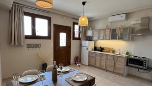 A modern kitchen with a dining area, featuring a wooden table set for two, a built-in oven, and a small island with a sink. - Tassos Cottage Fiskardo Kefalonia (Kefalonia)