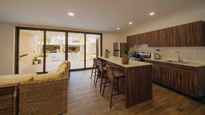 A modern kitchen with a central island, wooden cabinets, and a large sliding glass door leading to an outdoor area with a pool. - Beach House in Monterrico Guatemala (Taxisco)