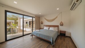 A modern bedroom with a large sliding glass door leading to a balcony, a wooden bed, and a small bedside table. - Beach House in Monterrico Guatemala (Taxisco)