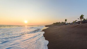 A beach with a sunset, palm trees, and beach huts. - Beach House in Monterrico Guatemala (Taxisco)