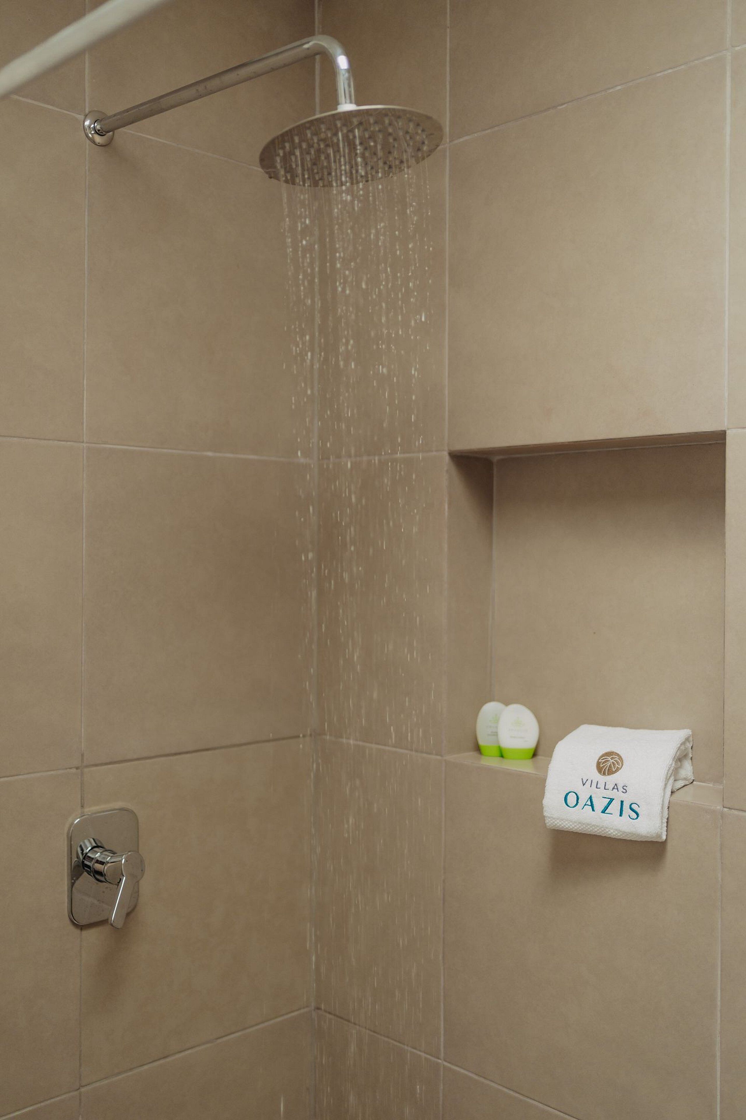 A shower with water running, a towel rack with a towel, and toiletries on the wall.