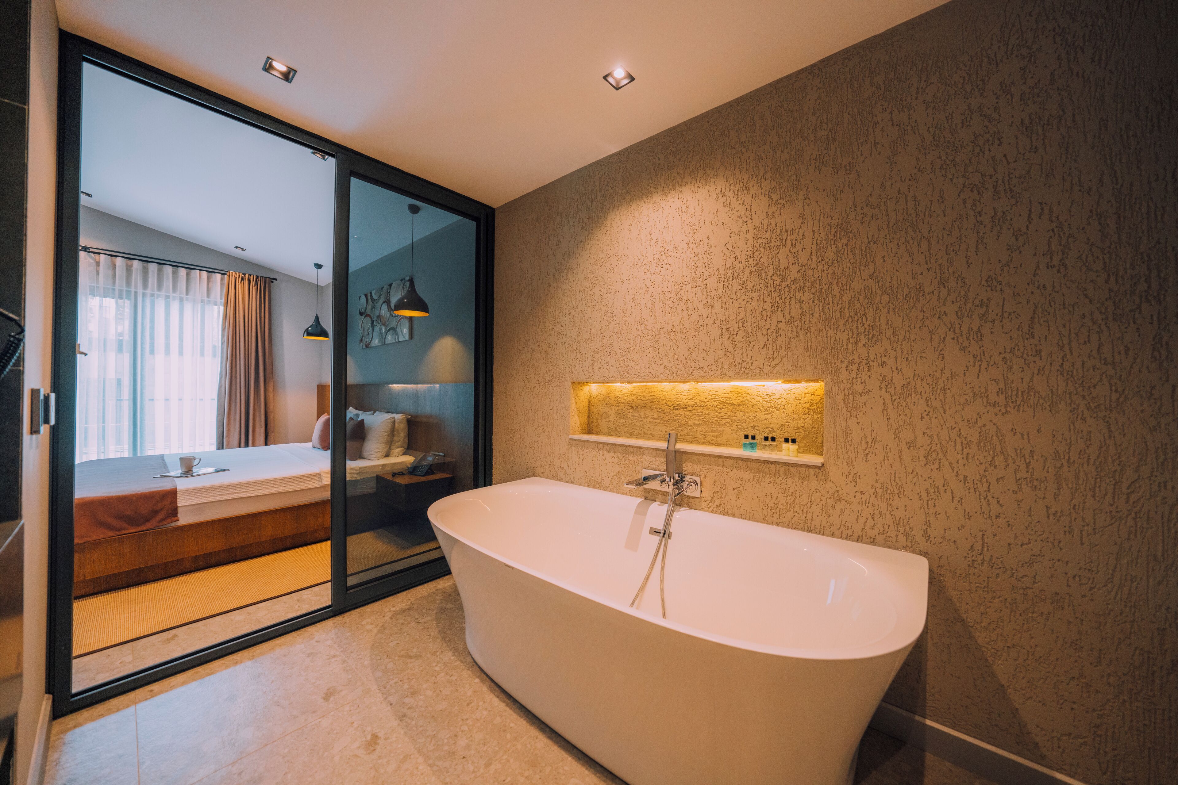 Een moderne badkamer met een vrijstaand bad, een douchecabine van glas en een wandlamp.