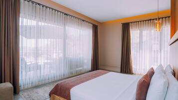 A modern hotel room with a large bed, wooden headboard, and a view of the outdoors through sheer curtains.