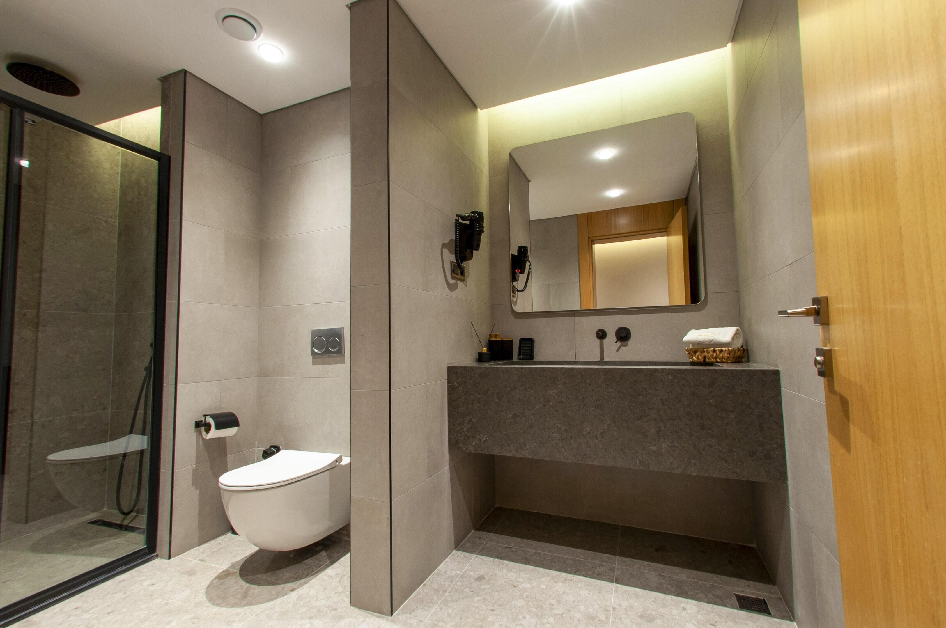 A modern bathroom with a freestanding toilet, a vanity with a mirror, and a shower area.
