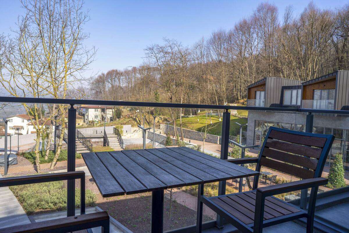 A balcony with a wooden table and bench, overlooking a residential area with houses and trees.