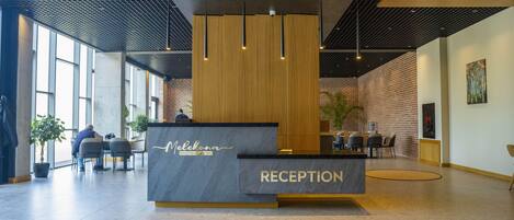 Moderne reception med skrivebord, siddeområde og store vinduer, der lukker naturligt lys ind.