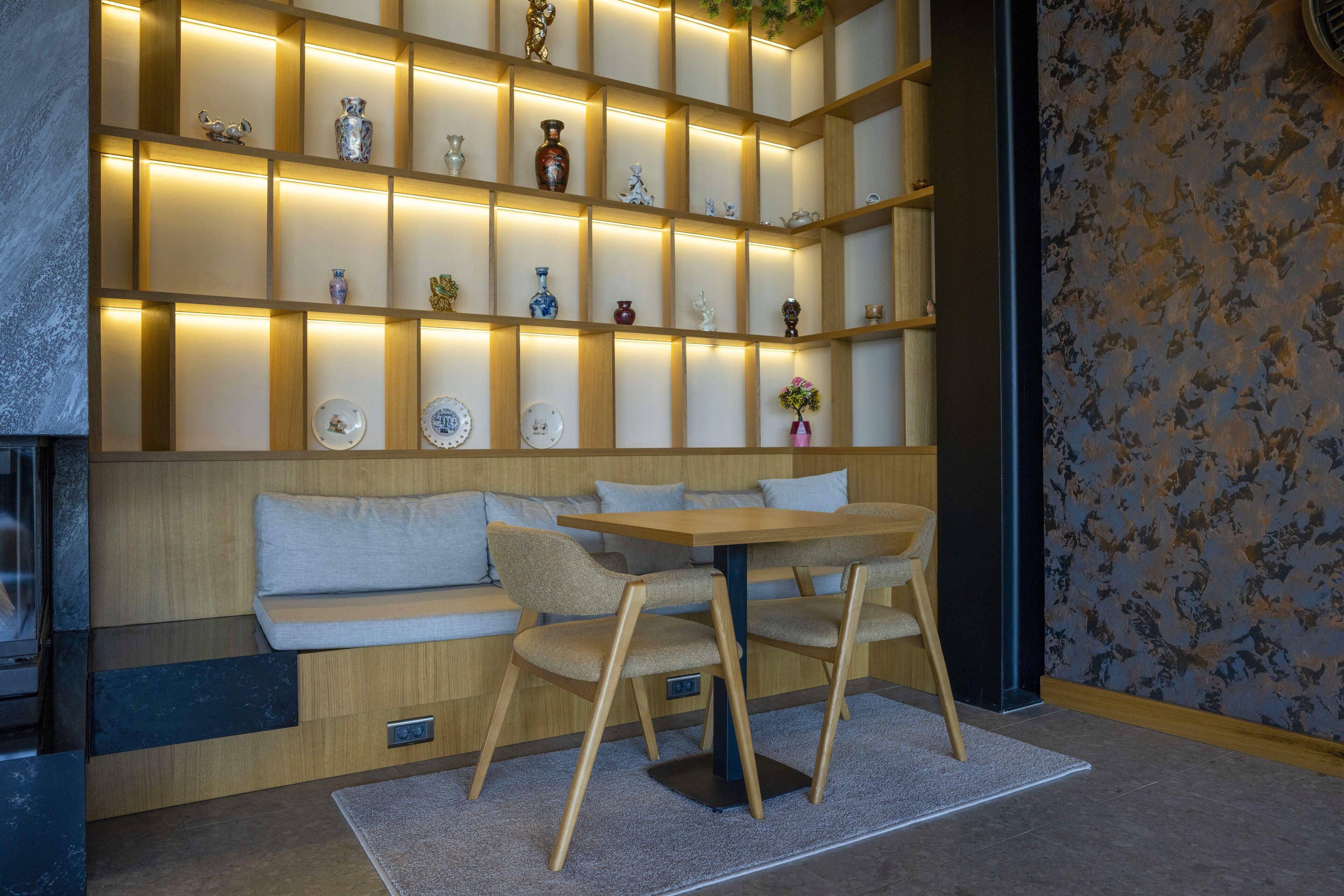 Un intérieur moderne avec un banc en bois, une table et des chaises. On peut voir des étagères ornées d’objets décoratifs.