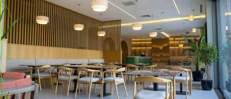 Interior moderno de restaurante con paneles de madera, varias mesas y sillas de comedor, iluminación colgante y una pared de ladrillo al fondo.