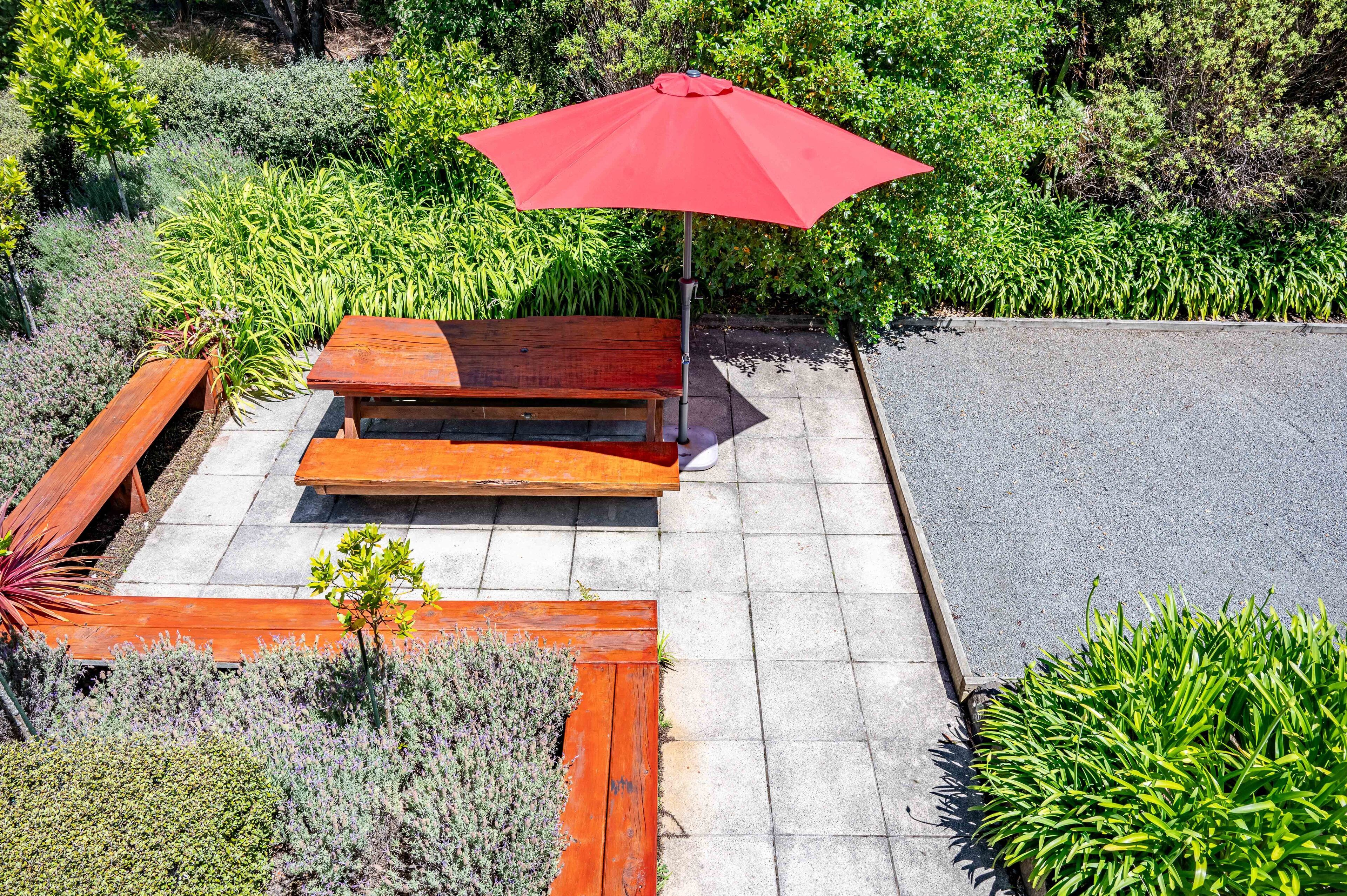 A patio area with a wooden bench and a red umbrella.