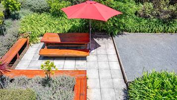 A patio area with a wooden bench and a red umbrella.