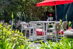 An outdoor dining area with a white table and chairs, a red umbrella, and a garden setting.