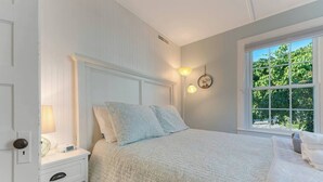 Un dormitorio con cama, mesitas de noche, lámpara y ventana con vista a árboles.