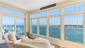 A room with large windows overlooking the sea, a sign reading "YORK BEACH MAINE", and a view of the ocean and distant buildings.