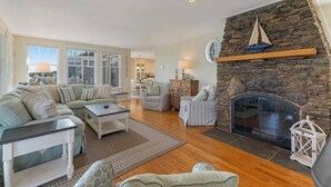 A spacious living room with a stone fireplace, a large window, and a cozy seating area. - Overlook Beach House #4- York Maine Beach Rental (York)