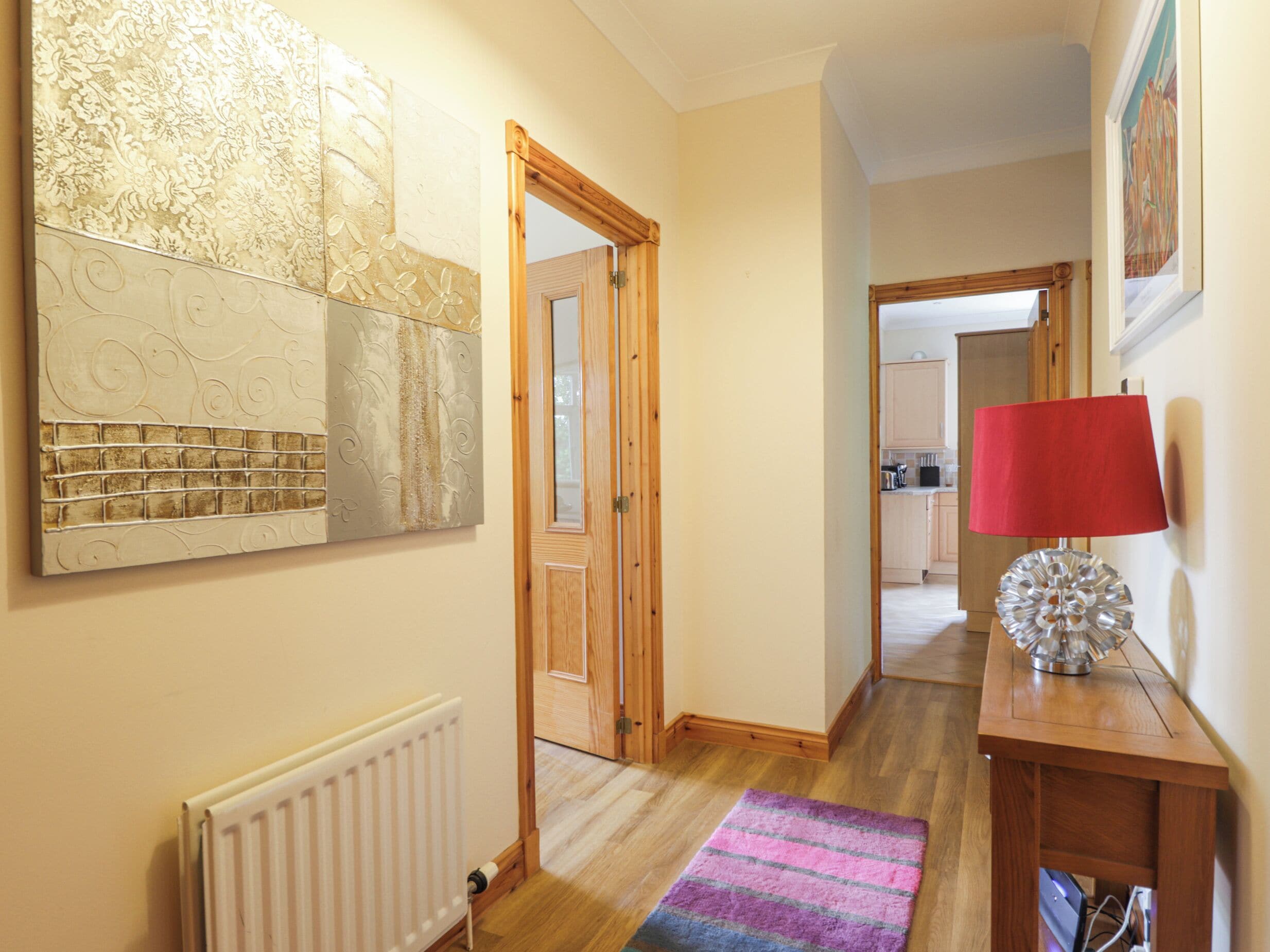 A hallway with a radiator, a wooden door, a rug, and a lamp on a wooden table.