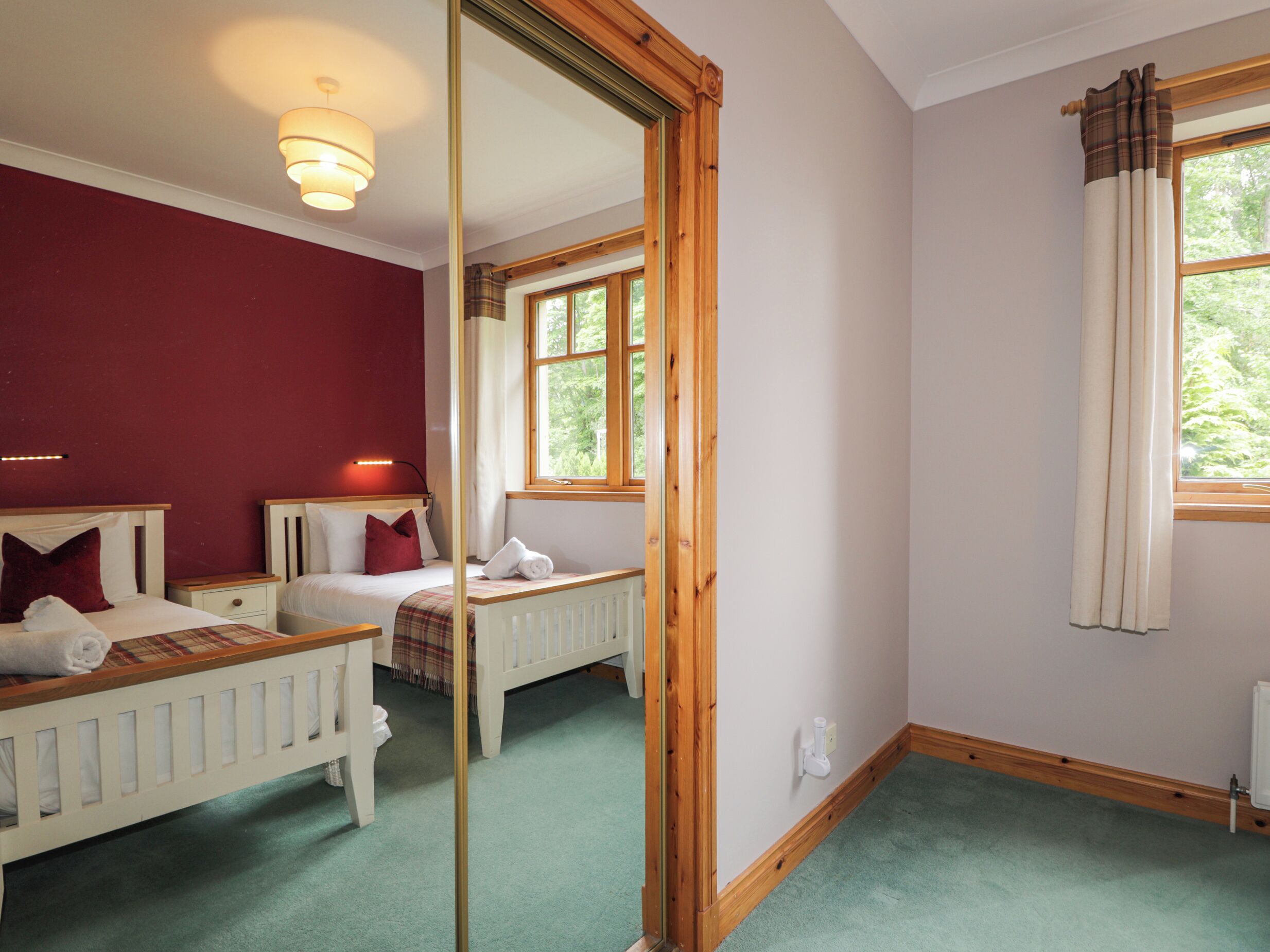 Ein Schlafzimmer mit zwei Betten, einem Spiegel, einem Fenster mit Vorhängen und einem Heizkörper.