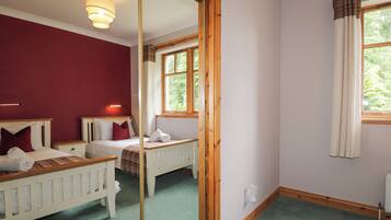 Ein Schlafzimmer mit zwei Betten, einem Spiegel, einem Fenster mit Vorhängen und einem Heizkörper.