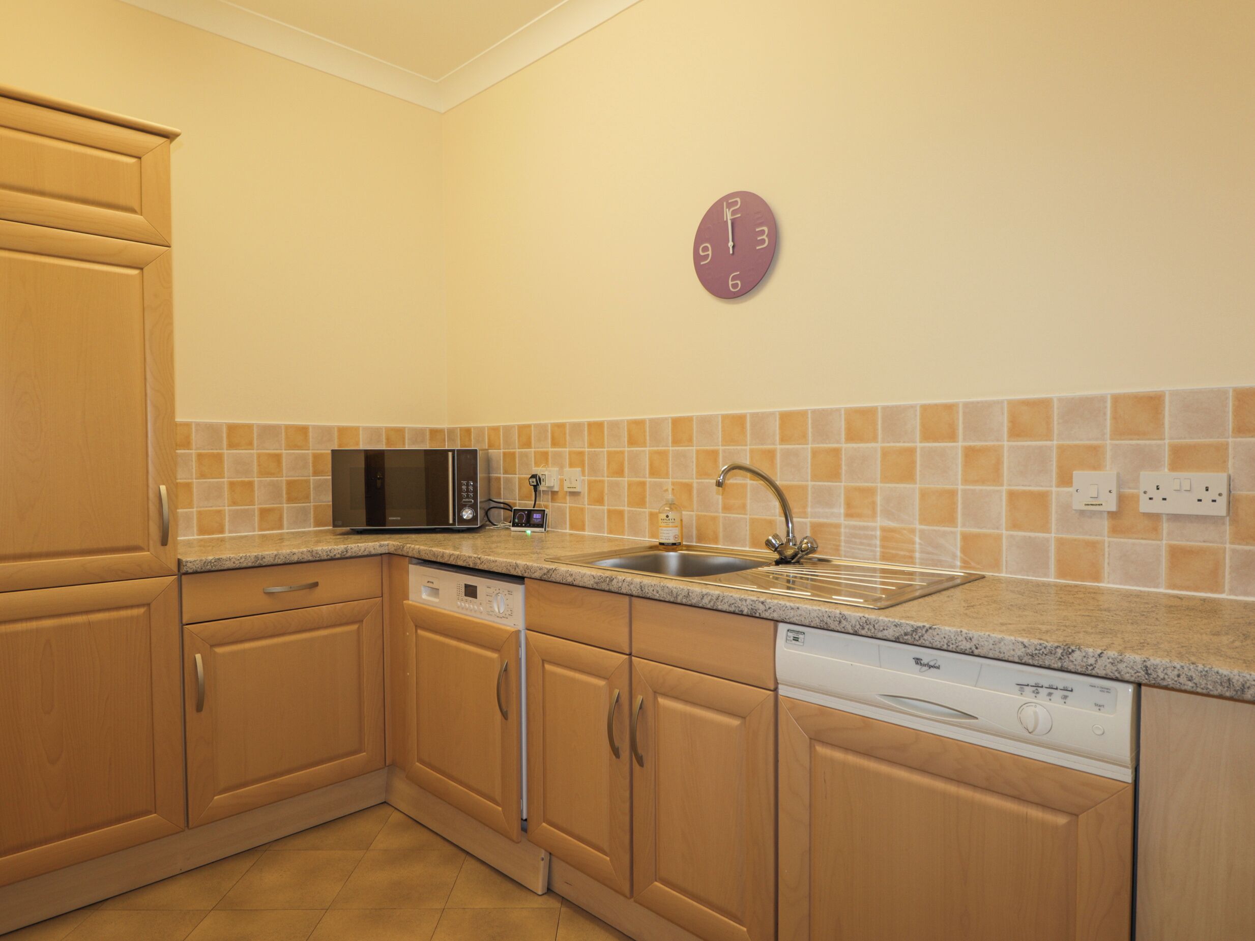 Una cocina con armarios de madera, microondas, lavavajillas y un lavabo con grifo.