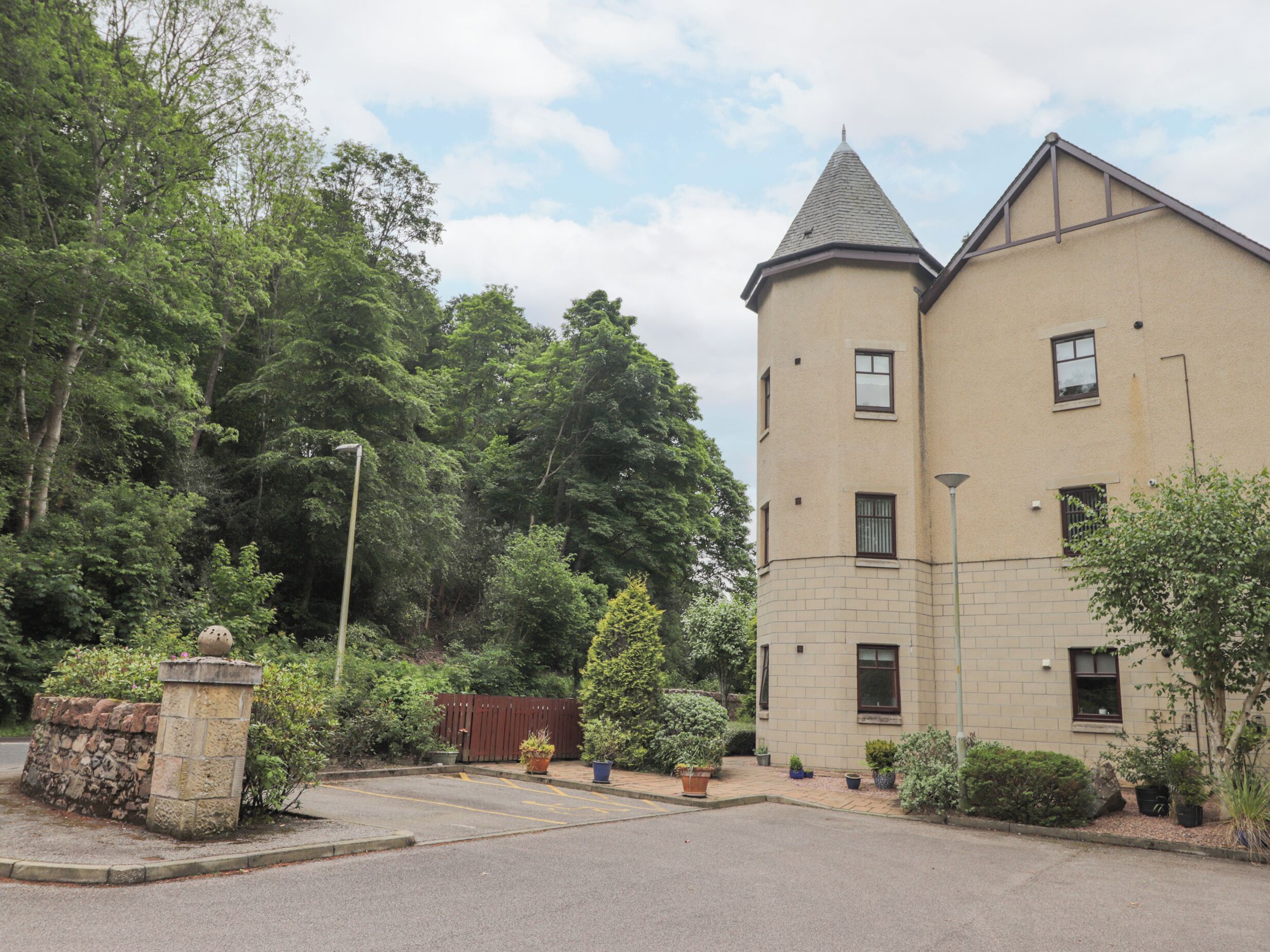 A two-story building with a tower-like structure, surrounded by lush greenery and a paved driveway.
