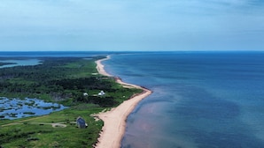 Luchtbeeld van een kustgebied met een strand, bebost gebied en een huis nabij de kust.